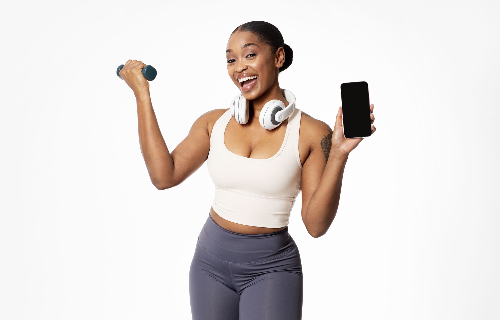 fit black woman with dumbbell shows phone empty screen, studio